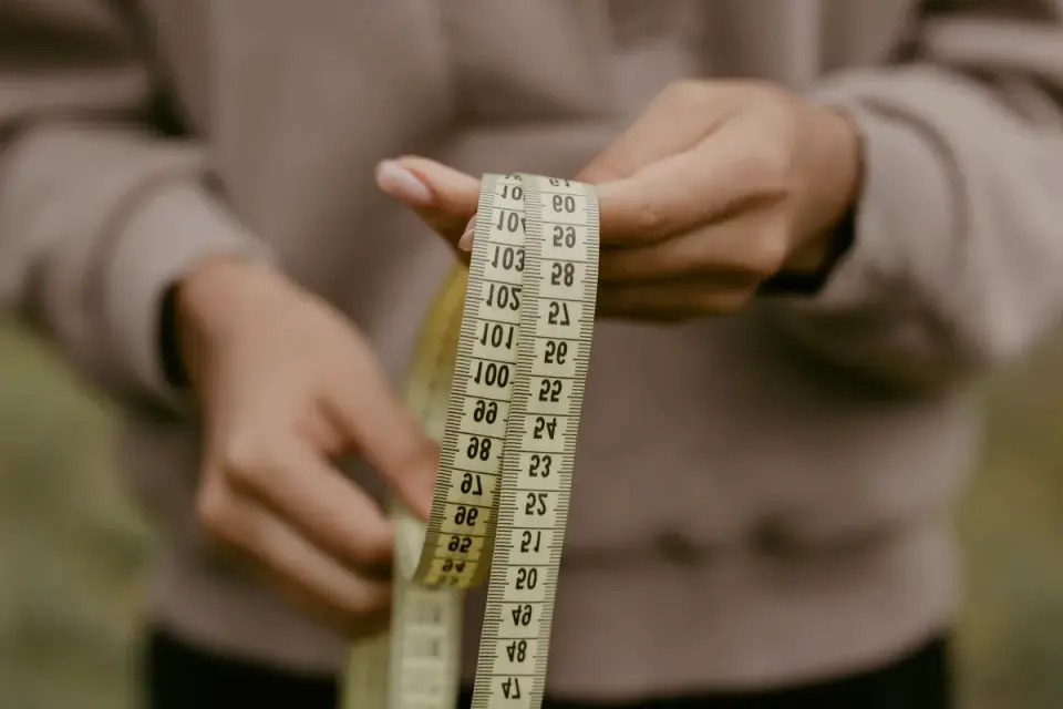 A person kneeling to measure a dog&#x27;s shoulder height with a soft tape measure