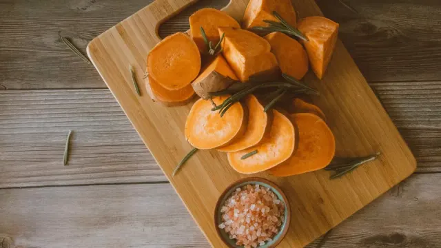 Cubed cooked sweet potato in a dog bowl next to a whole raw sweet potato on a counter