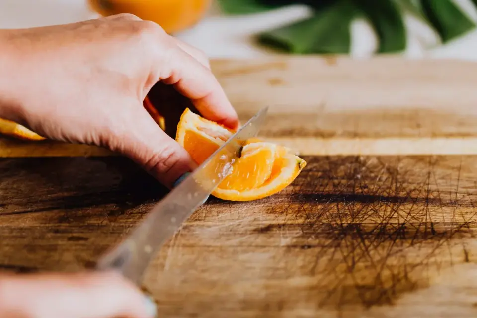 Hands peeling a sweet potato and cutting it into small cubes on a cutting board