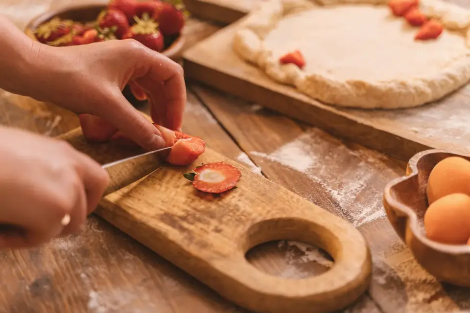 Small dog sniffing sliced strawberries on a wooden cutting board